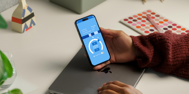 Person holding a phone showing a thermostat app.